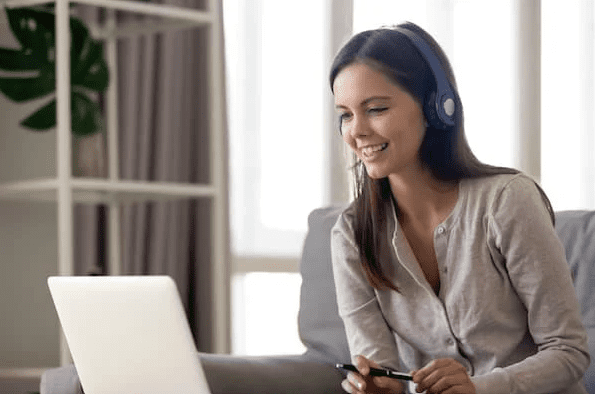 Woman with headphones using laptop on sofa.