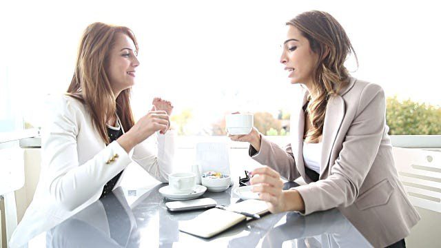 Two women in blazers having coffee and a chat.