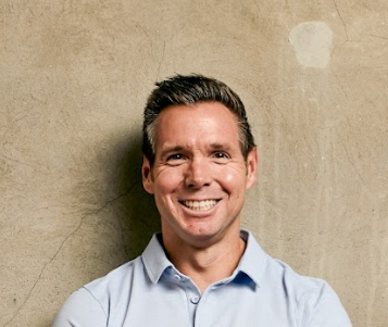 Smiling man in blue shirt against wall.