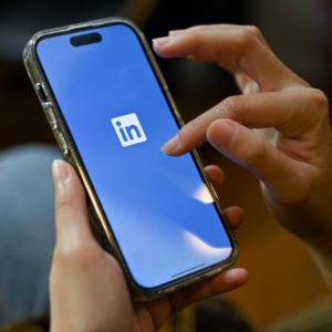 A hand holding a phone with the LinkedIn logo.