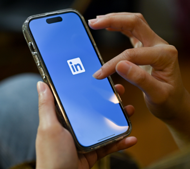 A hand holding a phone with the LinkedIn logo.