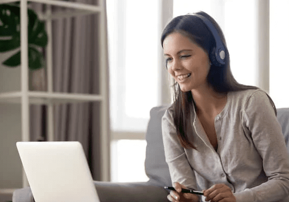 Woman with headphones using laptop on sofa.