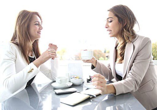 Two women in blazers having coffee and a chat.